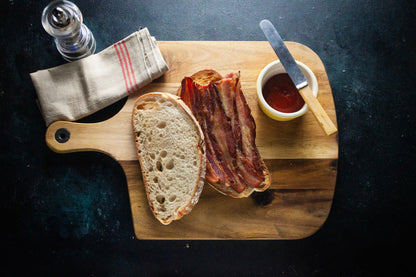 A bacon butty on a chopping board. The sandwich contains a generous helping of Aged Smoked Streaky Bacon
