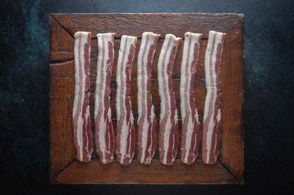 Uncooked rashers of streaky bacon on a wooden block.
