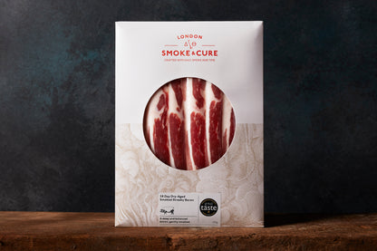 A pack of London Smoke & Cure's streaky bacon standing on a wooden surface with a dark background.